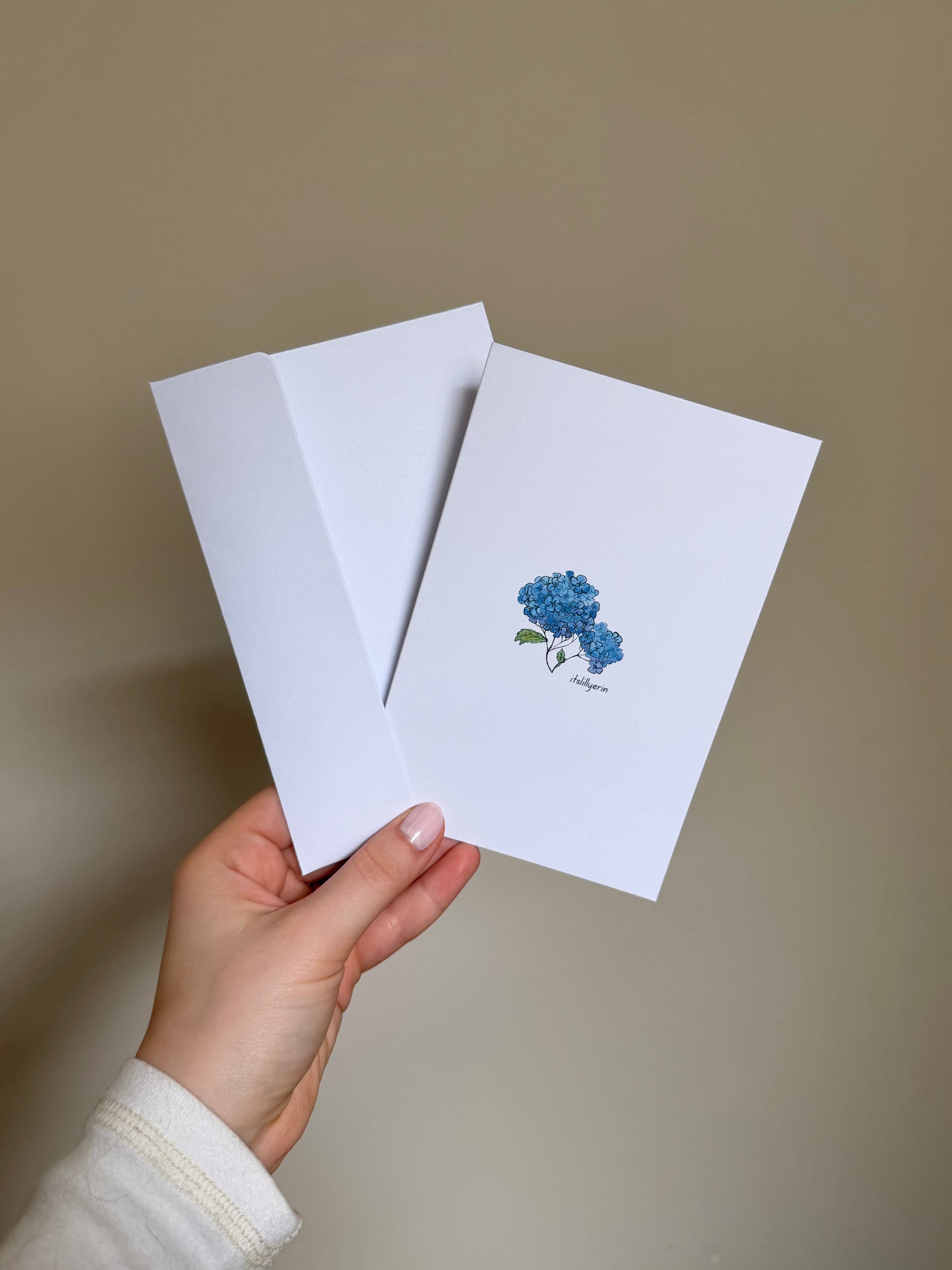 Hand holding a white card with a blue flower design on a beige background