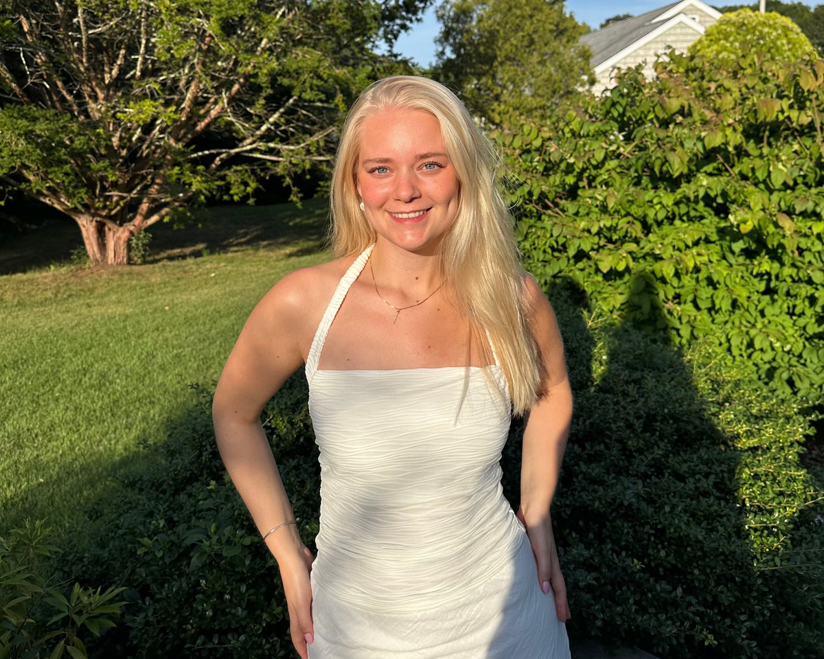 Woman in a white dress standing outdoors with greenery and a house in the background